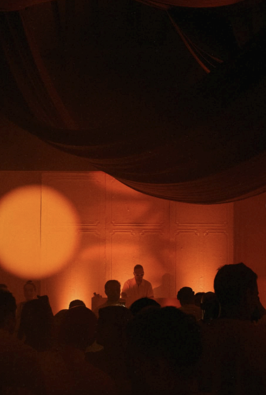 Amber-lit party scene with draped ceiling and guests gathered around the music