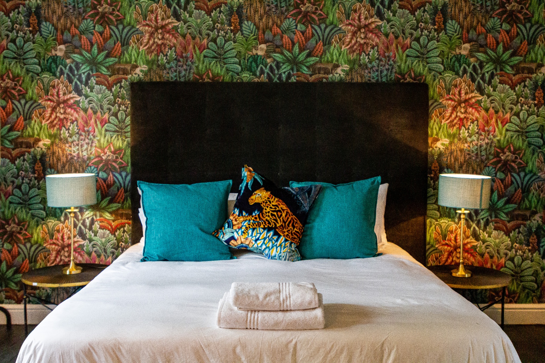 Merle Cottage bedroom detail with teal cushions and brass lamps