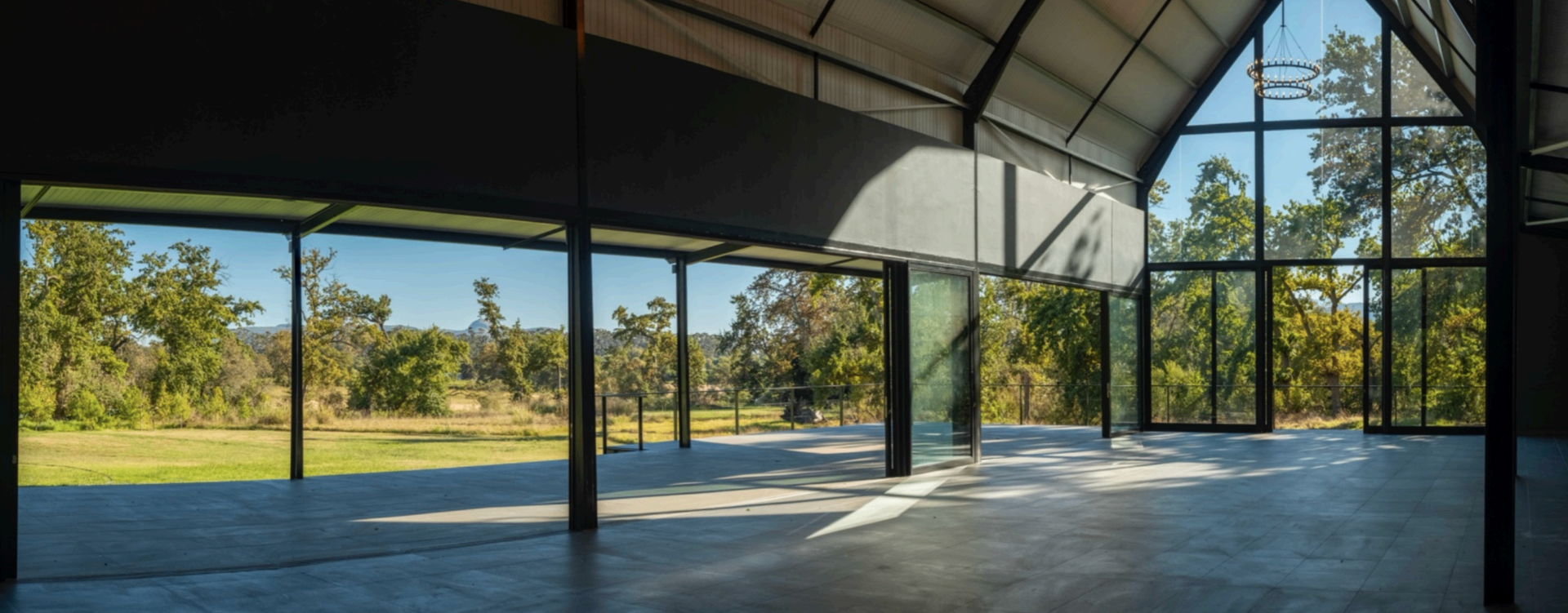 Light-filled glass pavilion venue with vaulted ceiling and chandeliers opening onto the gardens