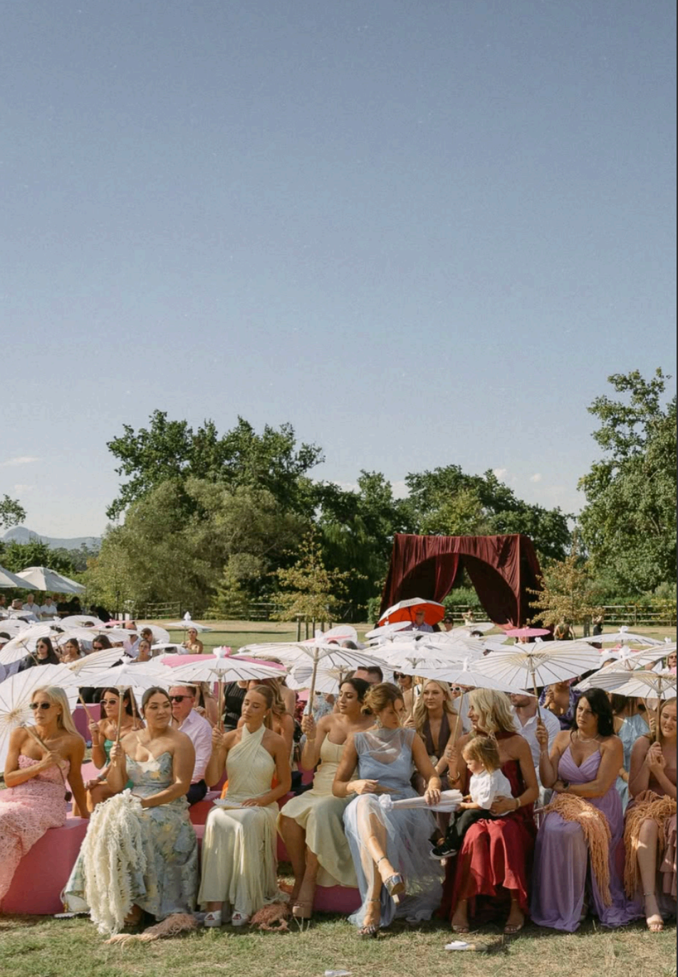 Guests seated outdoors with parasols during a summer ceremony